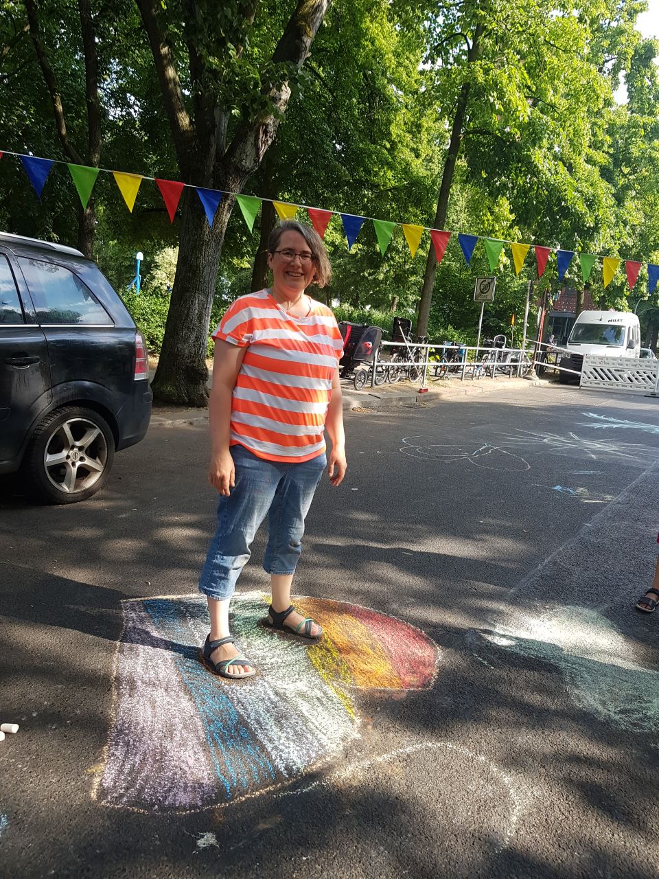 Corinna steht in einem gemalten Regenbogen Herz auf der Spielstrasse